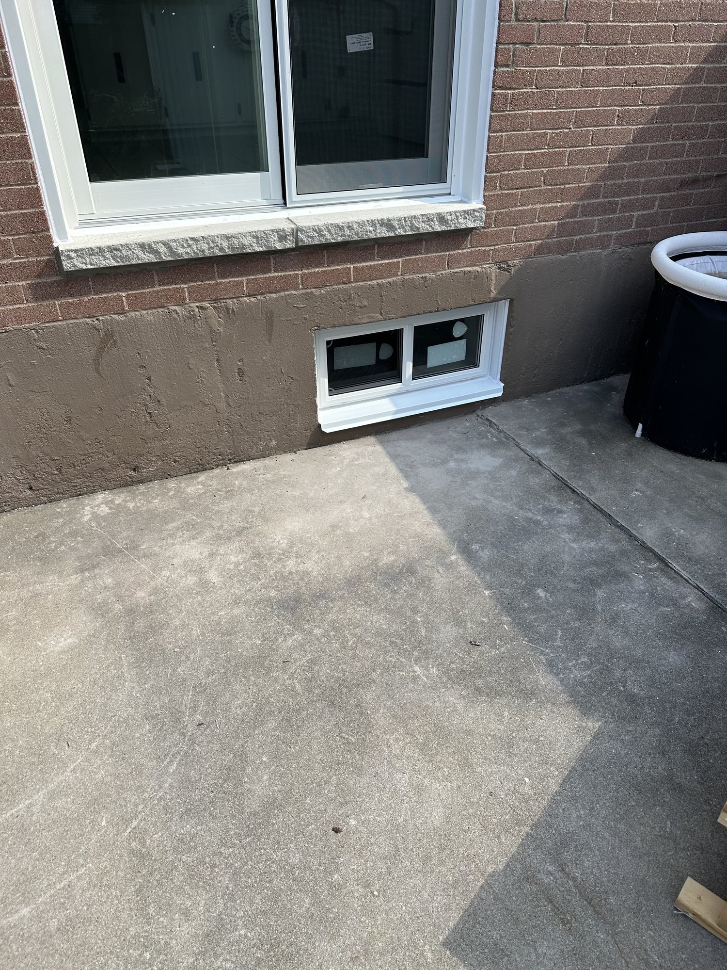 New white single-slider basement window in the foundation of a brick Hamilton home