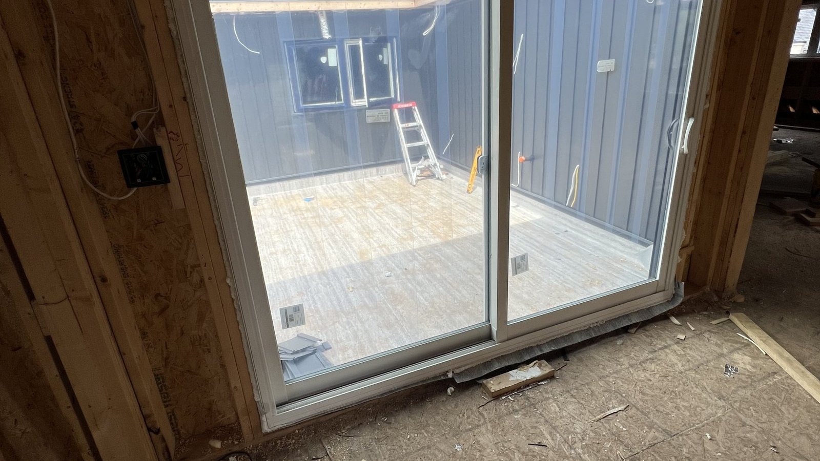 White sliding patio door viewed from inside an unfinished home addition